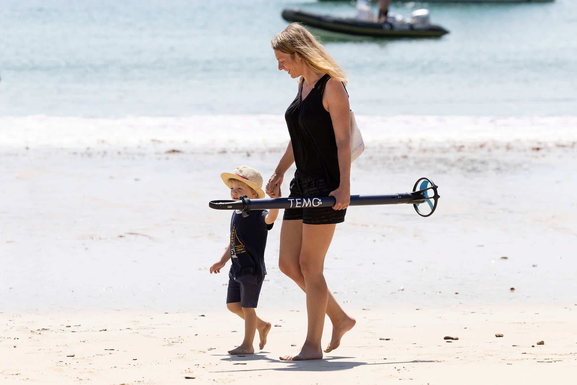Légèreté du moteur hors-bord TEMO·450 porté à une main par une personne sur la plage.