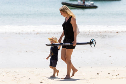 Légèreté du moteur hors-bord TEMO·450 porté à une main par une personne sur la plage.